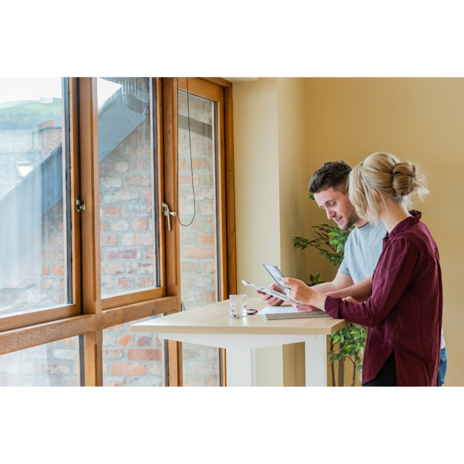 Man and woman collaborating at Quiet Motor Standing Desk by window reviewing paperwork
