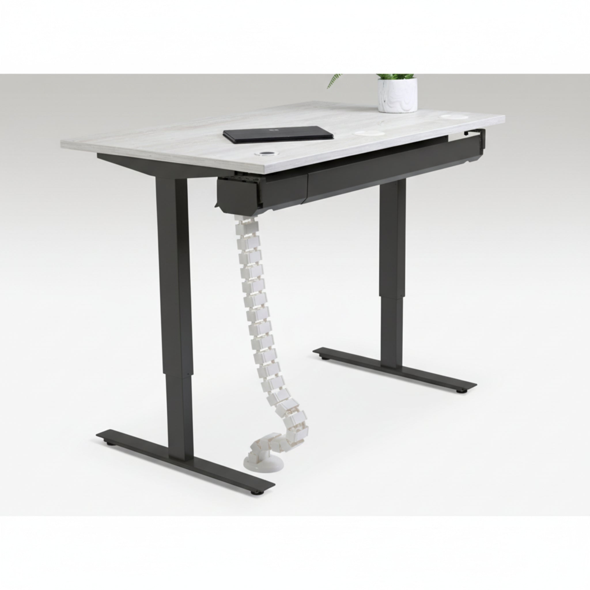 Quiet Motor Standing Desk with cable management feature shown holding device cords neatly with notebook and plant on desktop