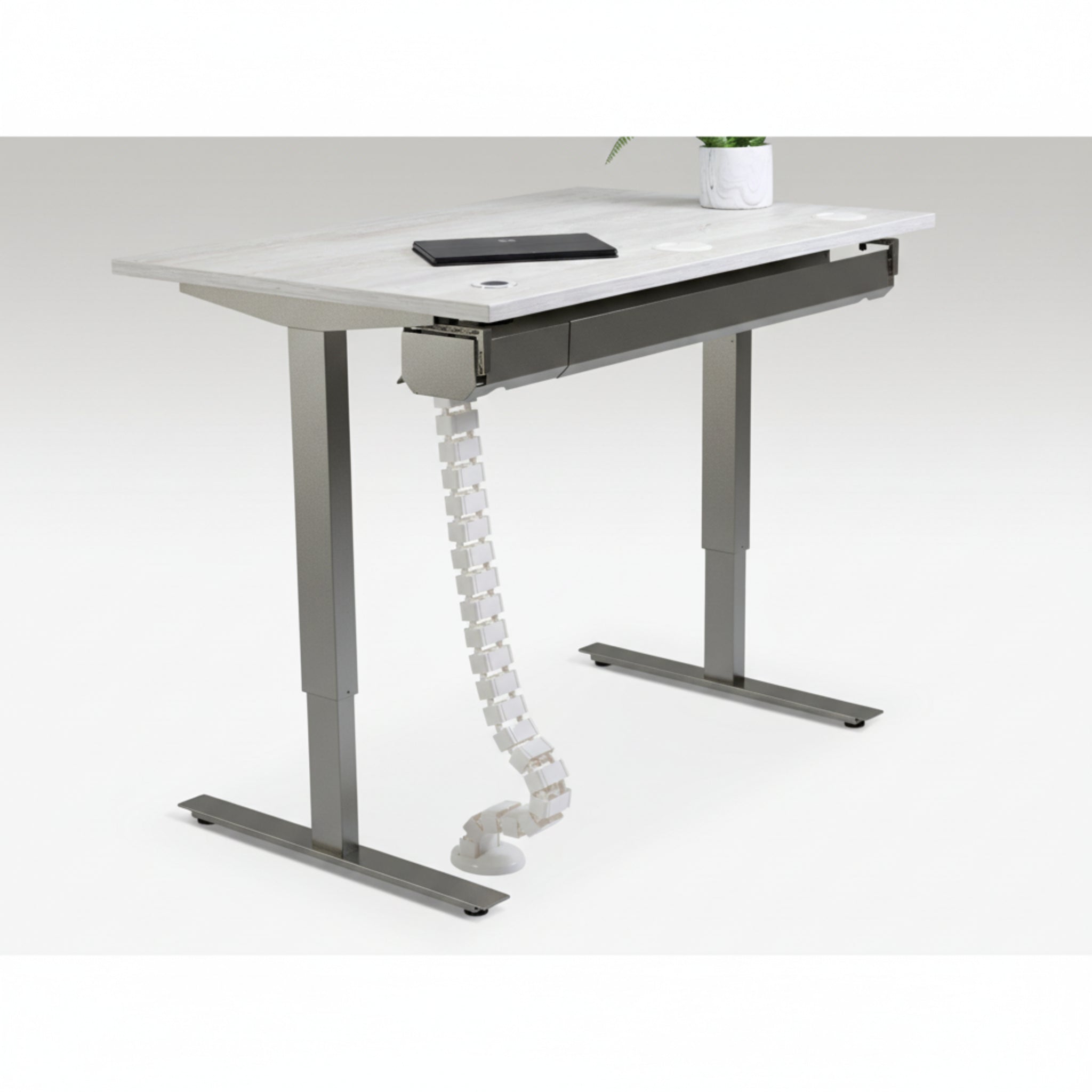 Quiet Motor Standing Desk with cable management feature shown holding device cords neatly with notebook and plant on desktop