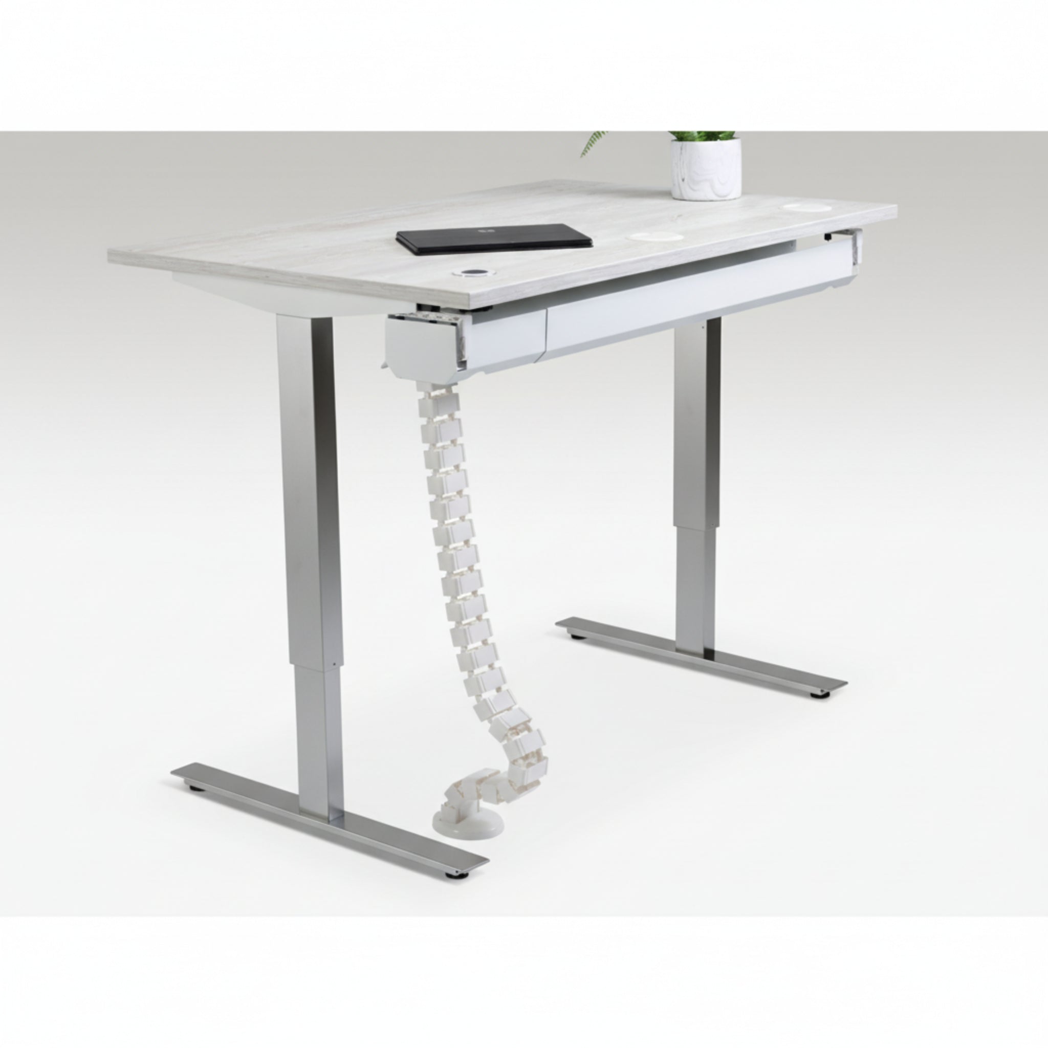 Quiet Motor Standing Desk with cable management feature shown holding device cords neatly with notebook and plant on desktop