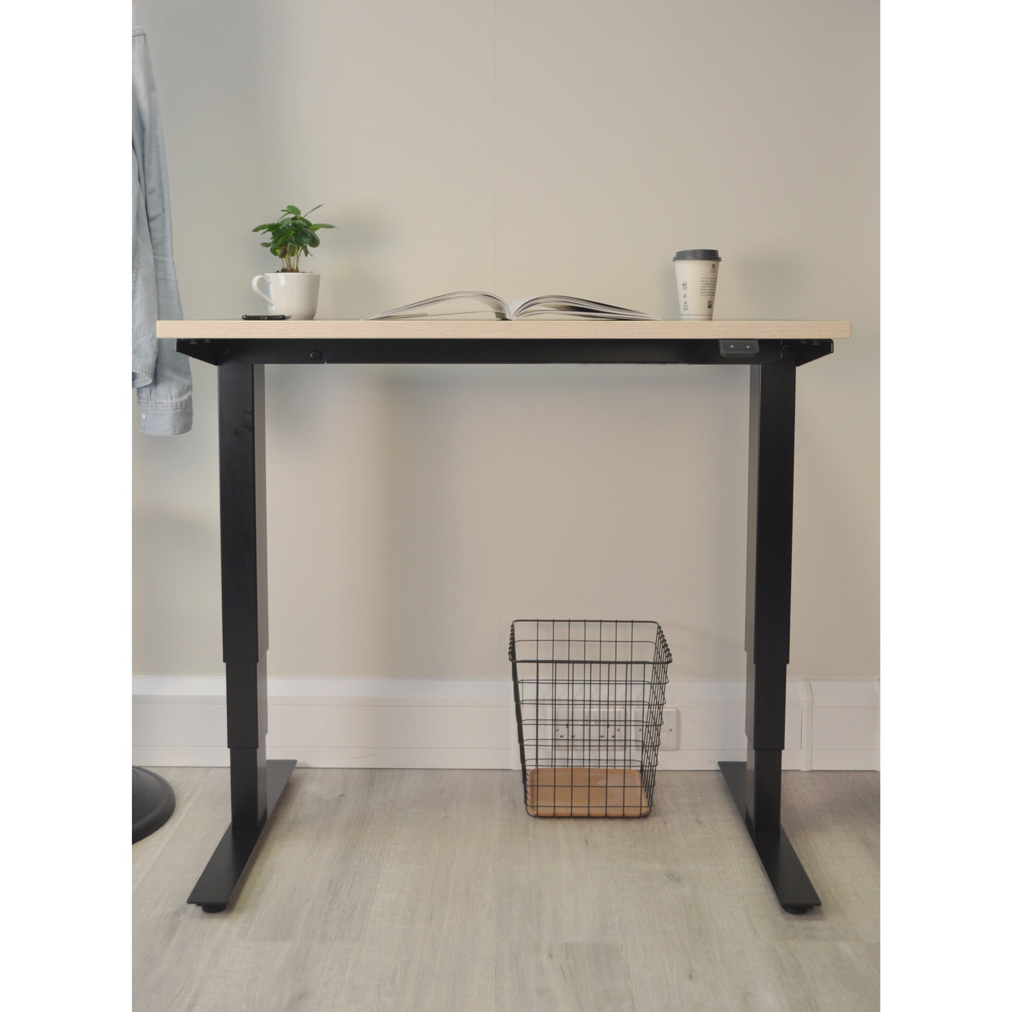 Black and light wood desk with a plant, book, and a cup on a light grey floor
