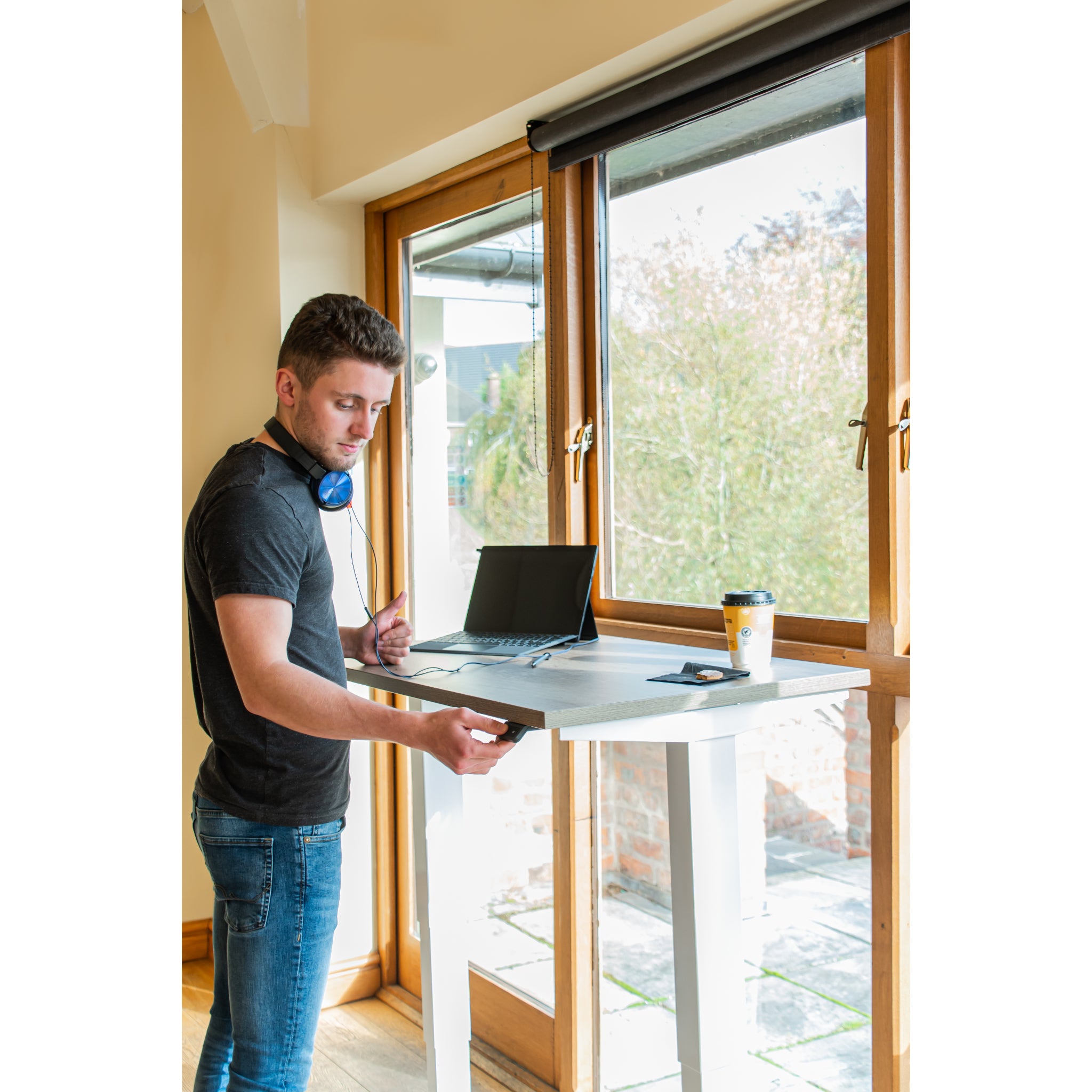 Person working on a laptop at a standing desk by a large window