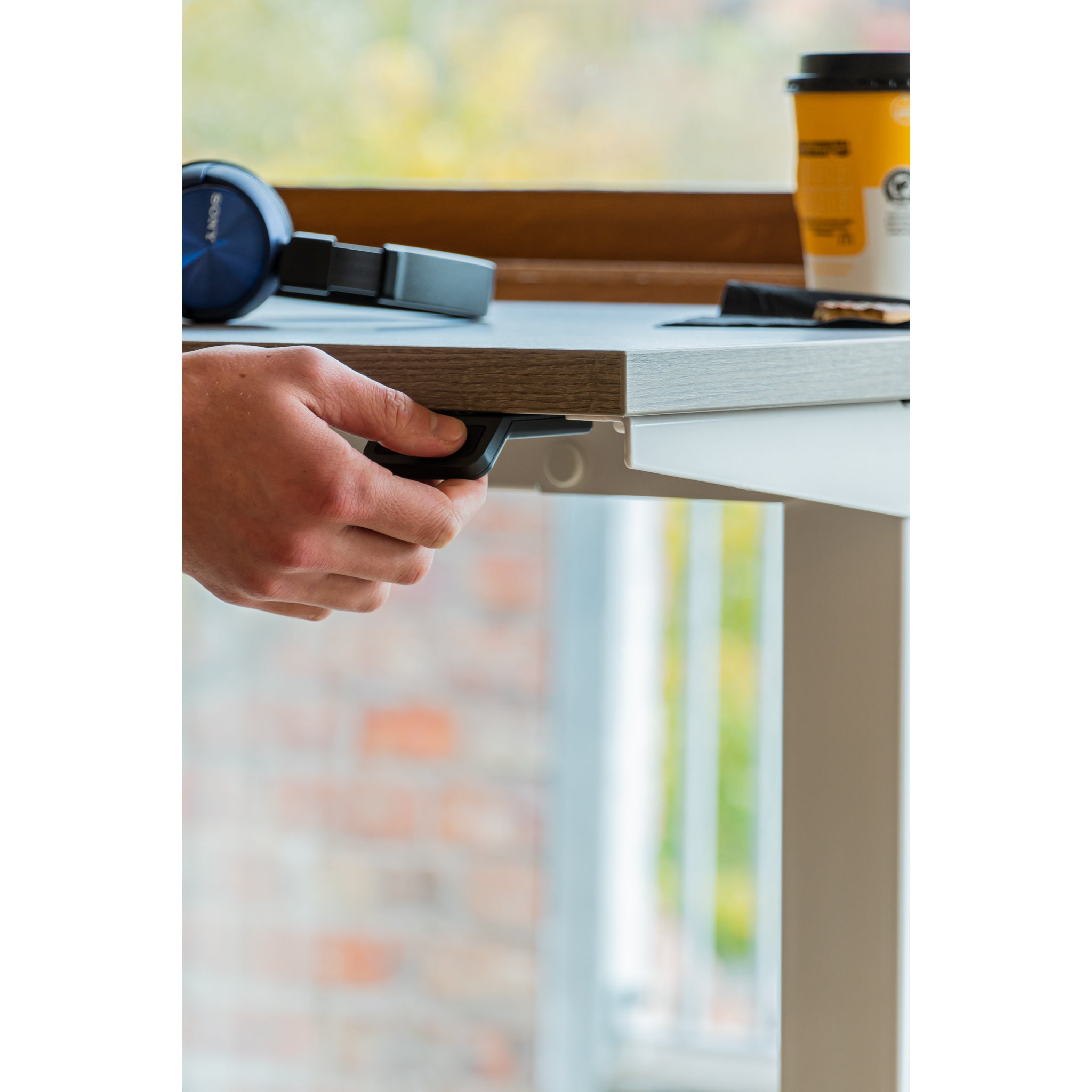 Person using desk controls with a coffee cup and headphones on a desk