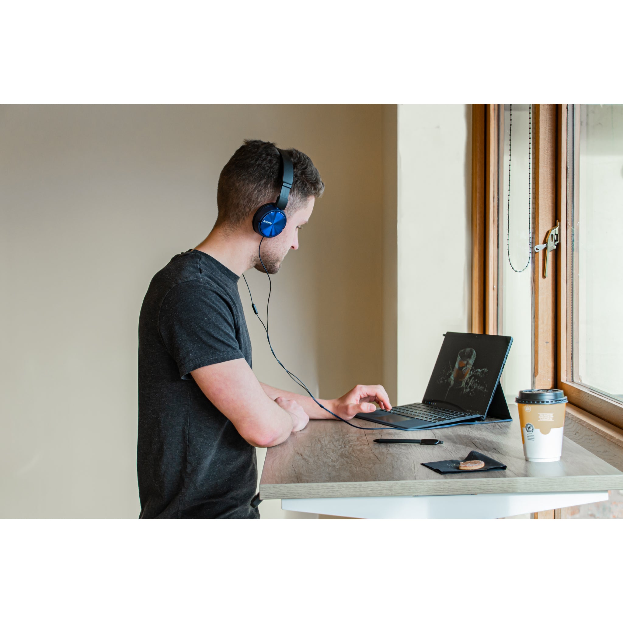 Person wearing headphones and using a laptop at a standing desk