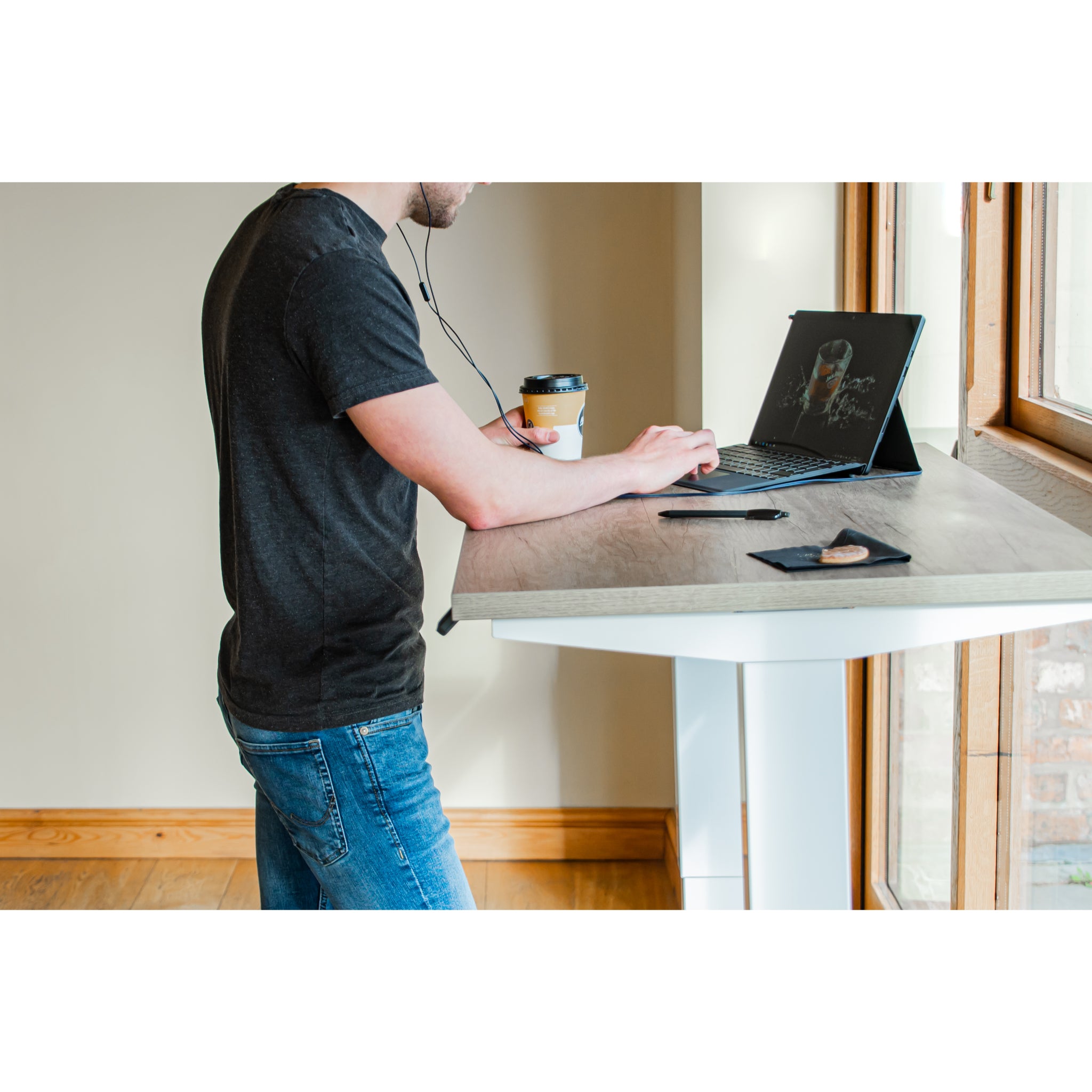 Person using a tablet with a coffee cup and phone on a compact white desk