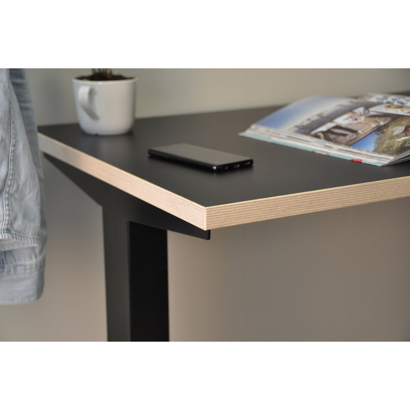 Close-up of UrbanErgo black standing desk with exposed plywood edge and modern black desktop in a compact workspace