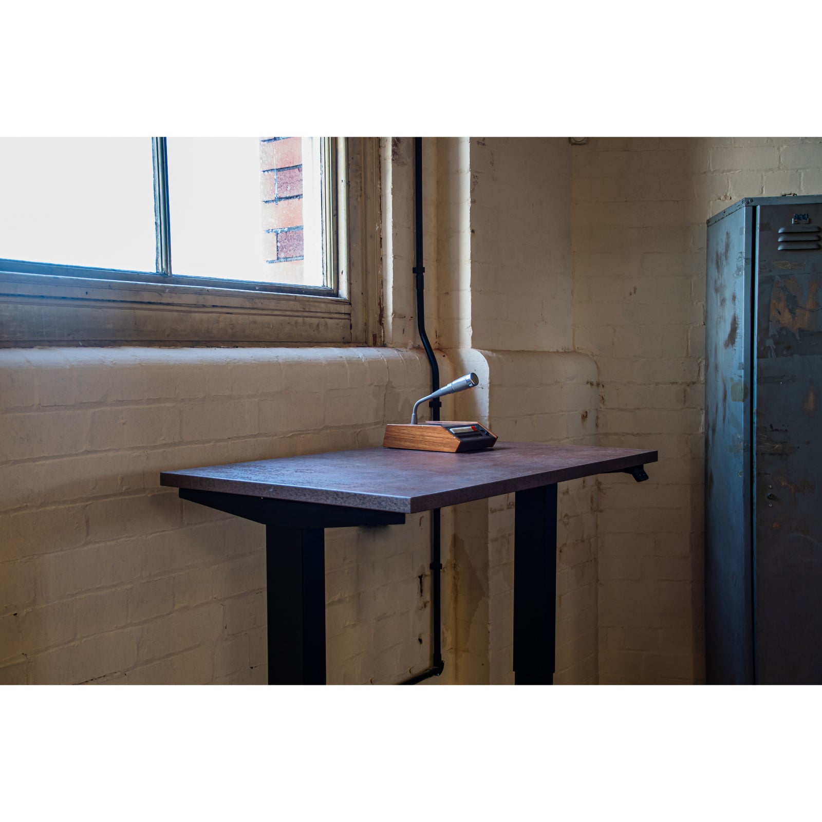 Industrial-style standing desk by UrbanErgo with brown desktop, set in a minimalist loft with exposed brick and mic accessory