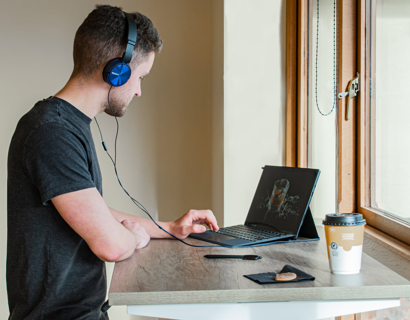 Man wearing headphones using a laptop at a sit-stand desk in a compact, modern workspace