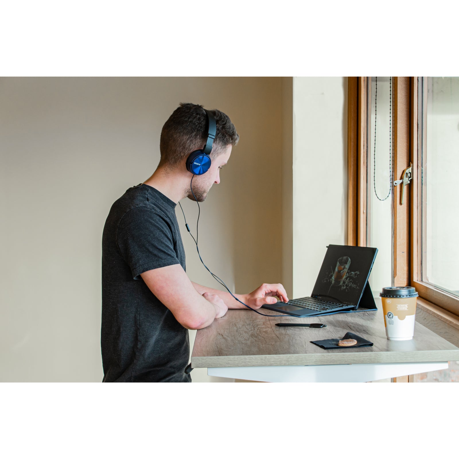 Man wearing headphones using a laptop at a sit-stand desk in a compact, modern workspace