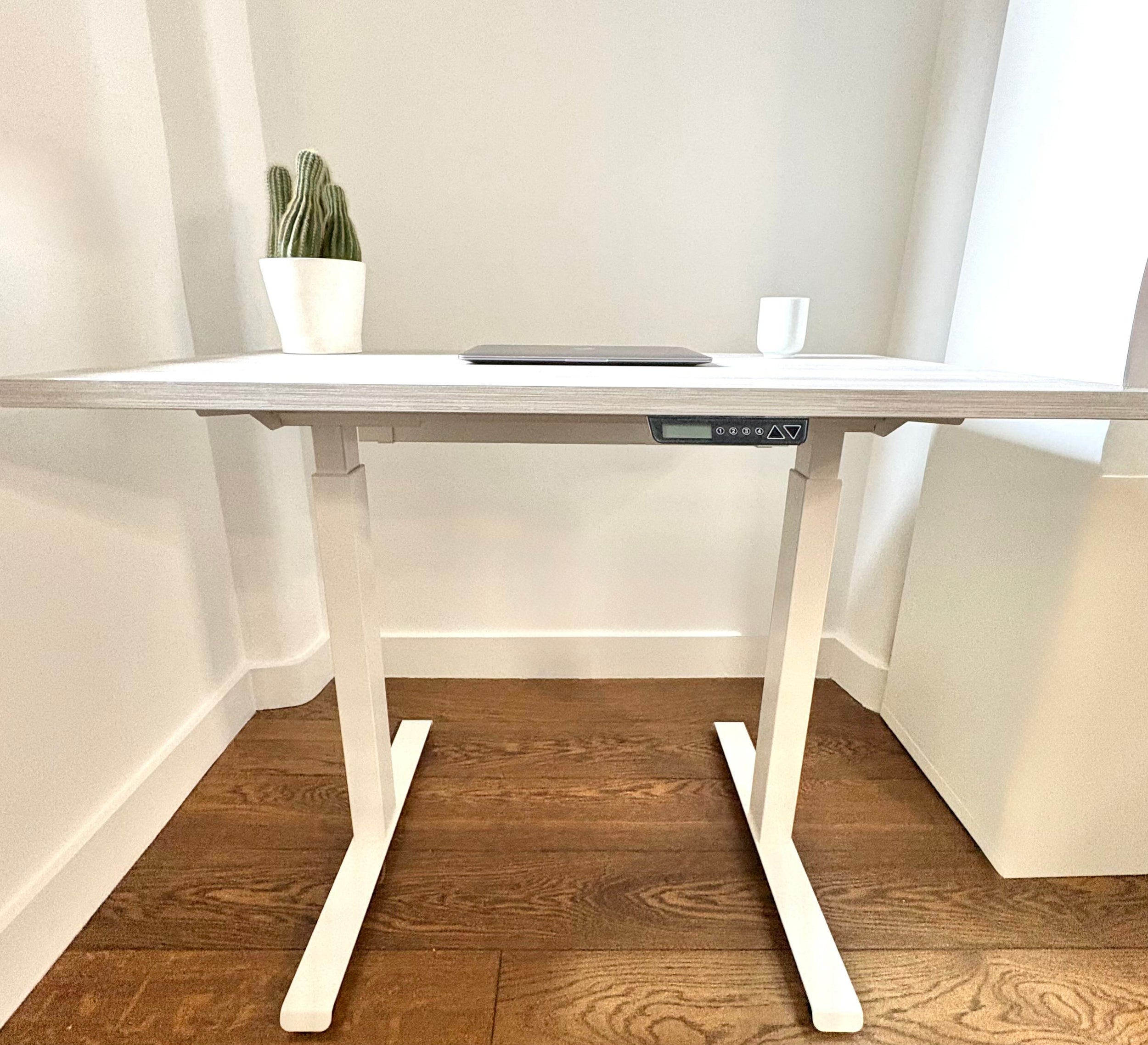 UrbanErgo Core electric standing desk with white frame and Casino Pine desktop styled in a compact home office