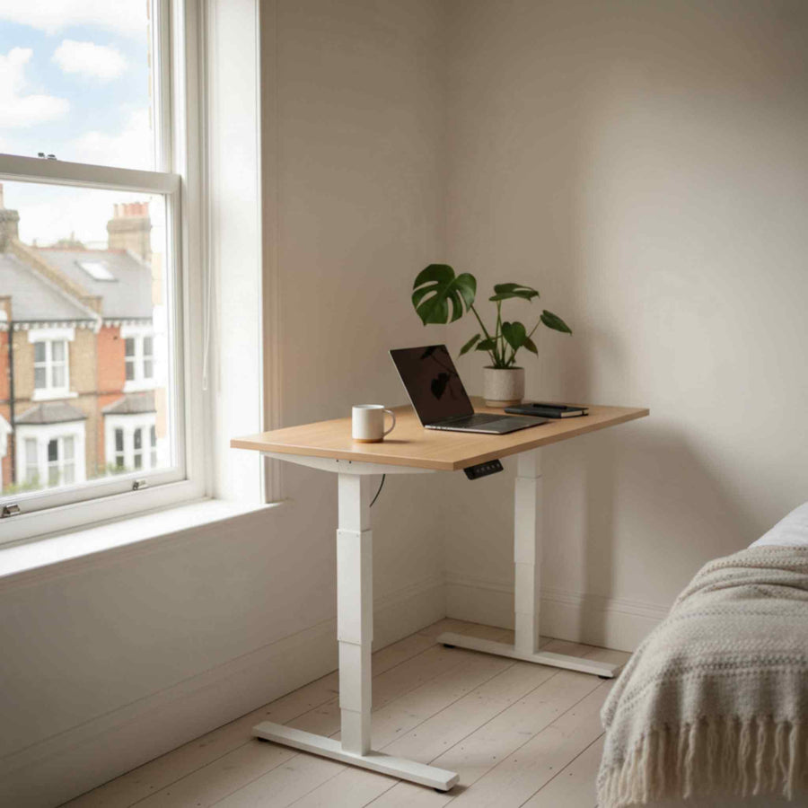 Scandinavian small-space standing desk with natural oak top and white frame, shown in a bright London flat workspace.